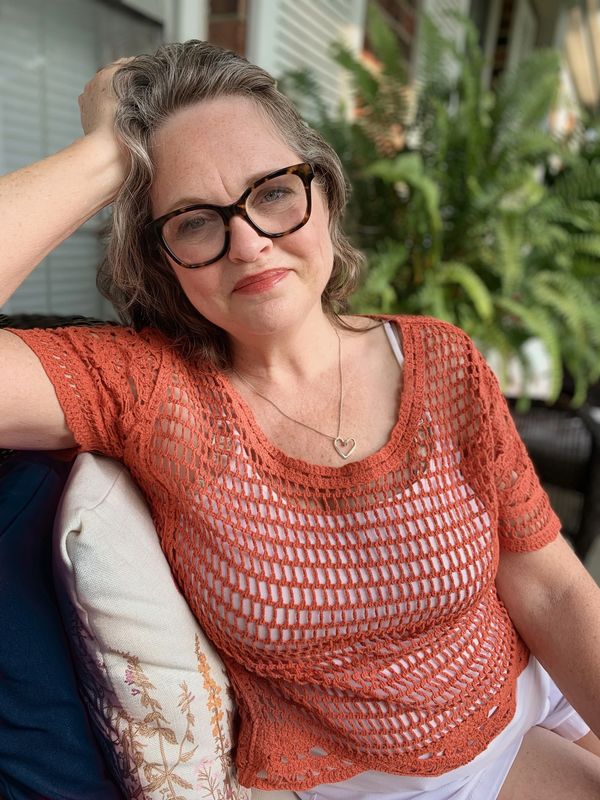 Smiling woman in glasses and a crochet top relaxing outdoors.