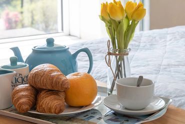 Teatray with yellowtulips in a vase & croissants in front of sunny window at Arallt Holiday Cottage