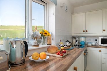 Clean bright kitchen at Arallt Holiday Cottage with sunflowers at window and generous welcome pack