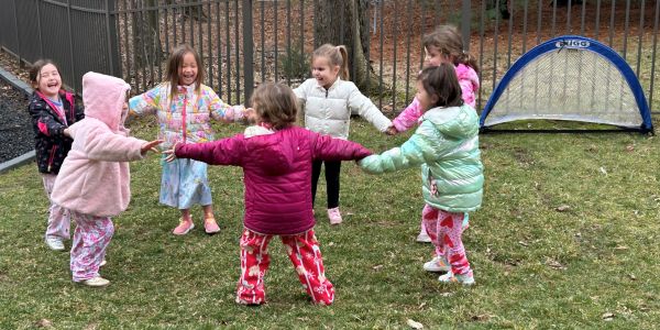 Children in colorful jackets holding hands and playing in a circle outside.