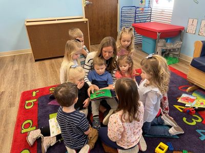 Teacher reading a book to a group of young children on a colorful rug.