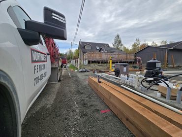 A fencing company truck parked at a construction site with lumber and pipes.