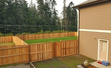 A wooden fenced backyard with a lawn and a beige house.