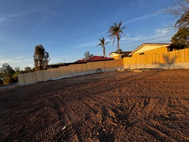 Cleared plot of land with fresh tire tracks under a blue sky near houses.