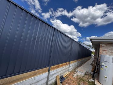 Long blue metal fence next to a house under a partly cloudy sky.