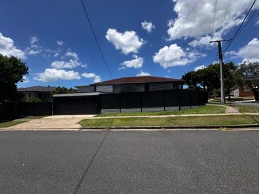 Modern suburban house with a black fence under a blue sky.