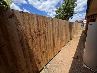 Long wooden fence beside a house under a partly cloudy sky.