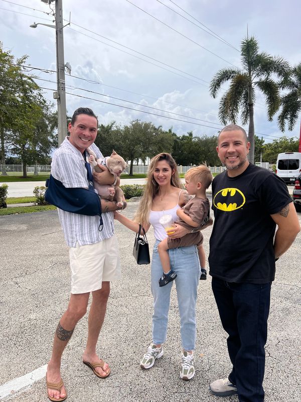 A cheerful group of four adults and a child outdoors, with one man holding a dog.