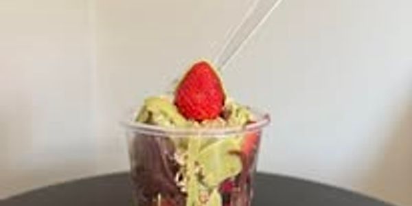 A cup of layered dessert with strawberry and green topping.