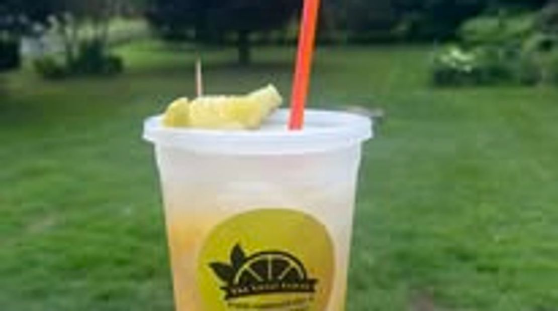 A cold pineapple drink in a plastic cup with a red straw outdoors.