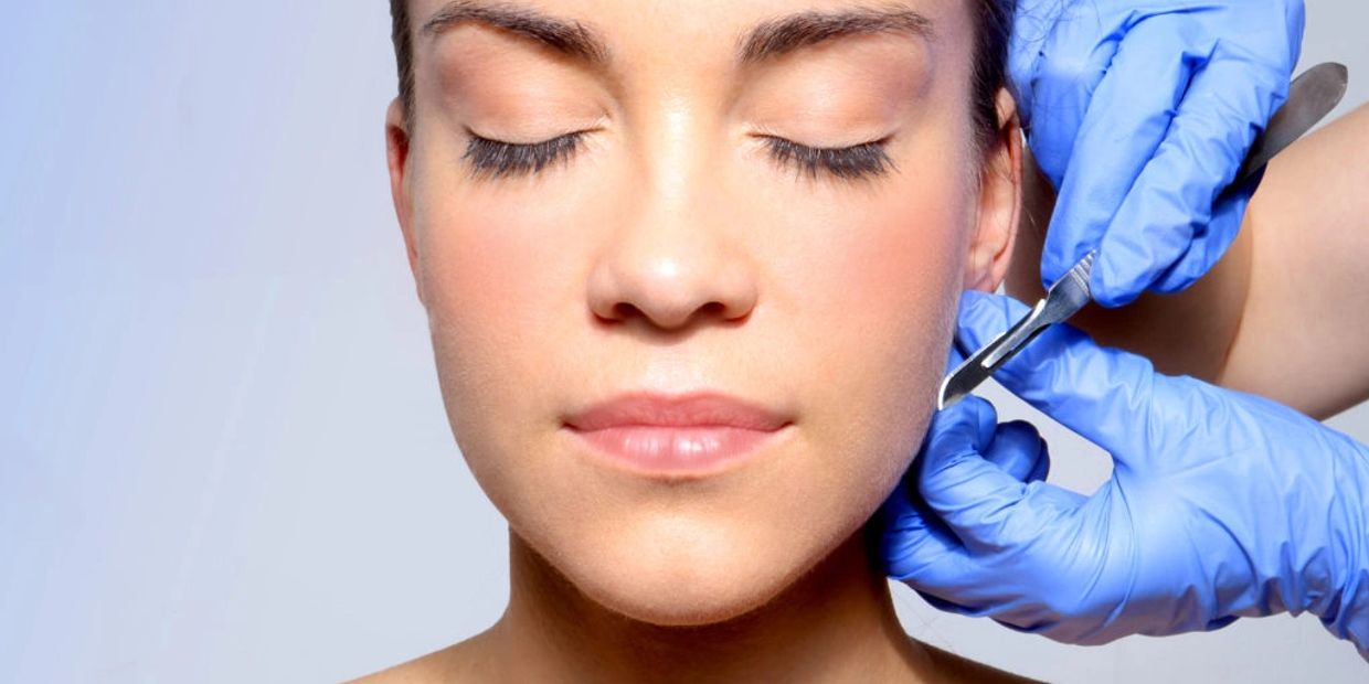 A woman receiving a cosmetic treatment on her jawline with blue-gloved hands.