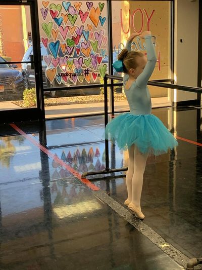 Young ballerina practicing in studio with colorful hearts on window.