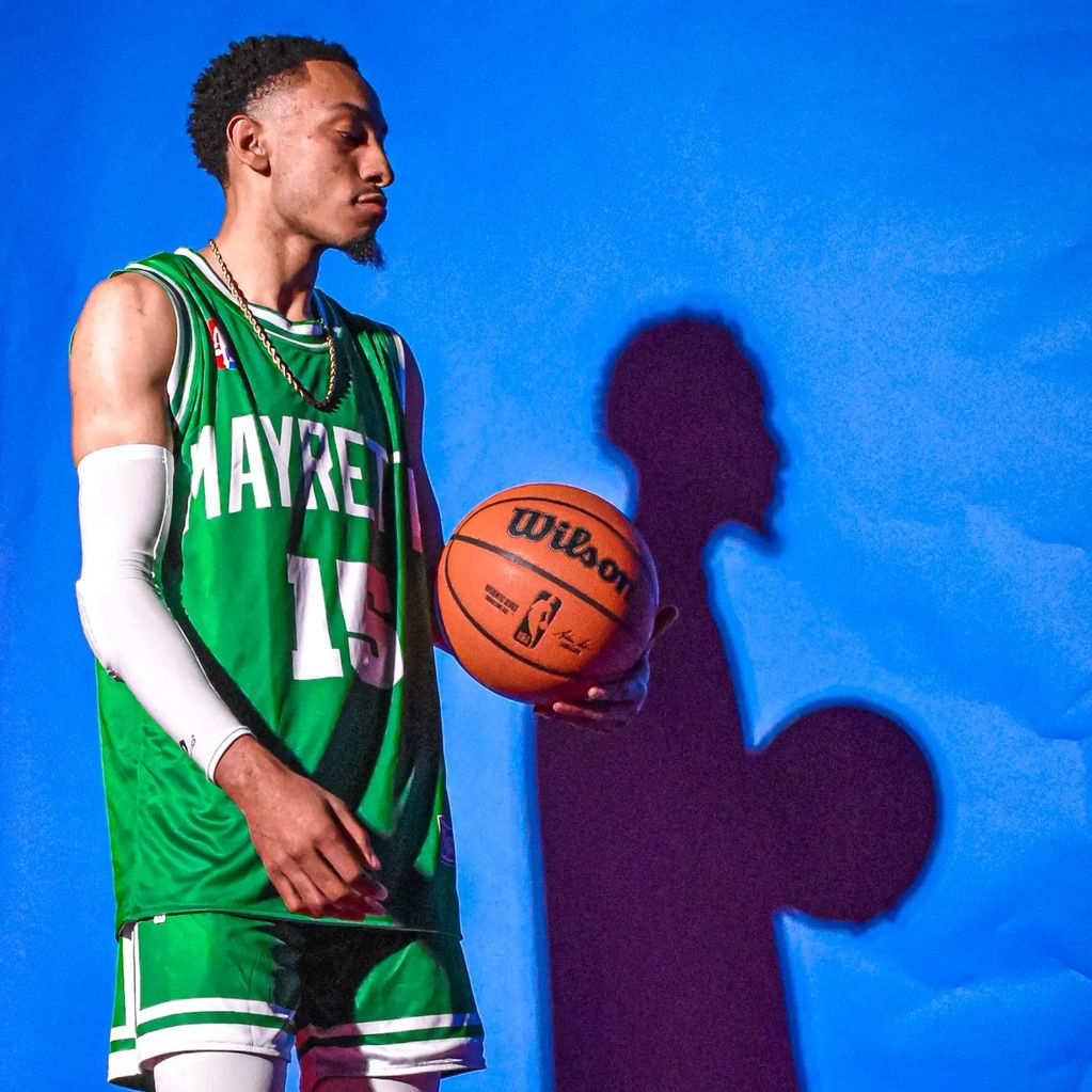 Basketball player holding ball, casting shadow on blue wall.