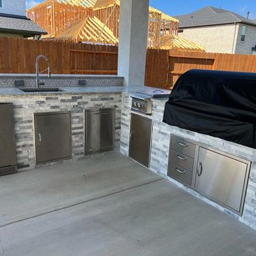 Modern outdoor kitchen with stainless steel appliances and stone countertop.