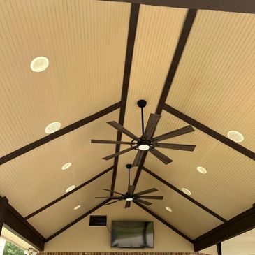 Covered patio ceiling with fans and a mounted TV above a brick wall.