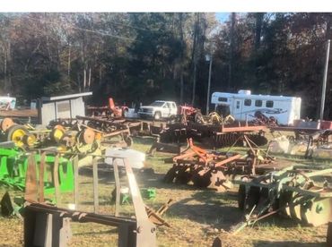 Outdoor farm equipment and machinery parts scattered on grassy field.