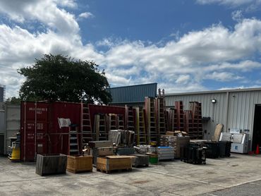 Outdoor storage area with ladders, crates, and equipment under a partly cloudy sky.