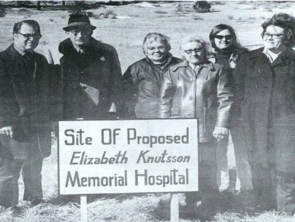 Group standing behind a sign for proposed Elizabeth Knutsson Memorial Hospital.