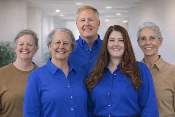 Five smiling adults, three in blue shirts, posing indoors.
