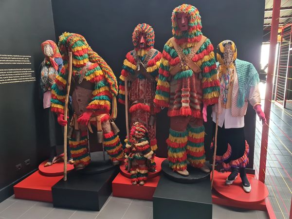 Traditional colorful costumes with masks and staffs on display in a museum.