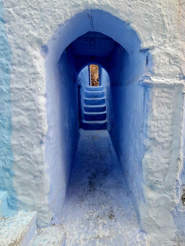Narrow blue passageway with arch and stairs leading upward.