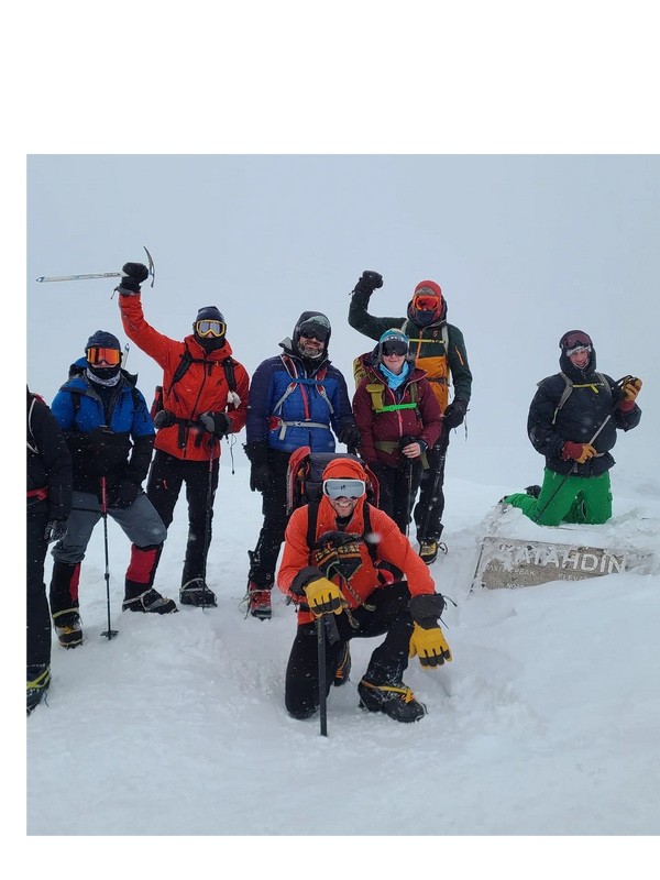 Group of climbers posing on a snowy mountain peak with ice axes and winter gear.