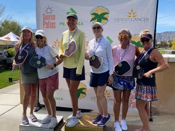 Group of people posing with medals and paddles at a pickleball event.