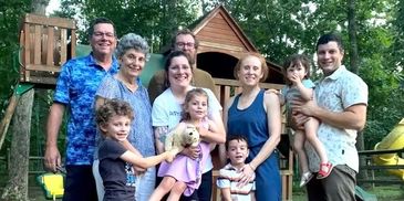 A happy family group posing outdoors near a wooden playset in a backyard.