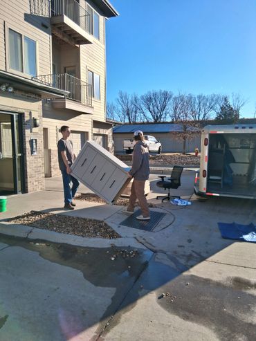 Two men moving a large cabinet outside a residential building.