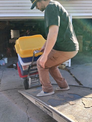 Man using a hand truck to move stacked storage bins up a ramp.