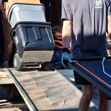 Two movers transporting bins and boxes down a ramp from a truck.