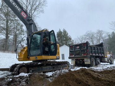 Excavator and dump truck on a snowy day digging a foundation