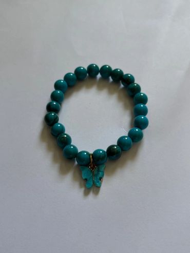 Turquoise beaded bracelet with a butterfly charm on a white background.
