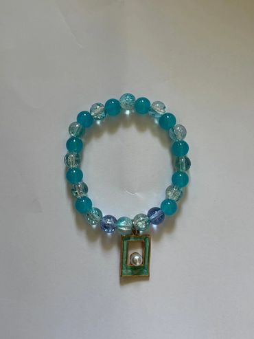 Beaded bracelet with blue and clear beads and a rectangular charm with a pearl.