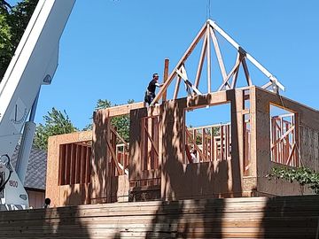 Construction workers framing a wooden house structure under a clear blue sky.