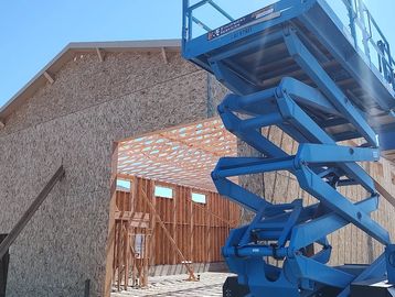 Construction site with wooden framing and a blue scissor lift under a clear sky.