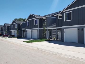 Row of modern two-story townhouses with gray siding and white trim under a clear blue sky.