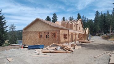 A wooden house under construction surrounded by trees and construction materials.