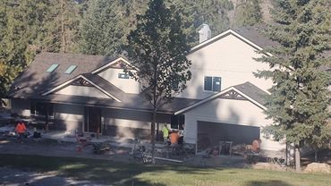 Large two-story house under construction surrounded by trees and mountains.