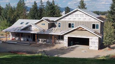 Large two-story house under construction surrounded by trees and mountains.