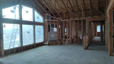 Interior of a house under construction with exposed wooden framing and large windows.
