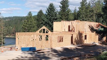 Wooden framed house under construction near a forested river.