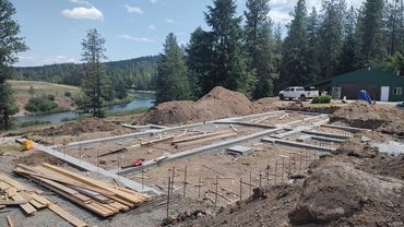 Construction site with building foundation near a river and forest.