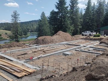 Construction site with building foundation near a river and forest.