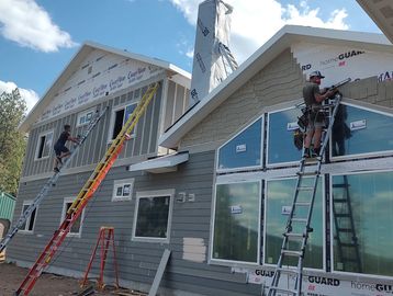 Two workers installing siding on a house using ladders on a sunny day.