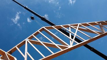 Wooden roof truss being lifted into place on a house under construction.