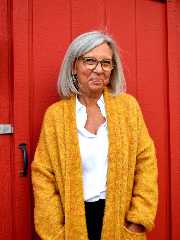 Smiling woman in glasses wearing a yellow cardigan against a red door.