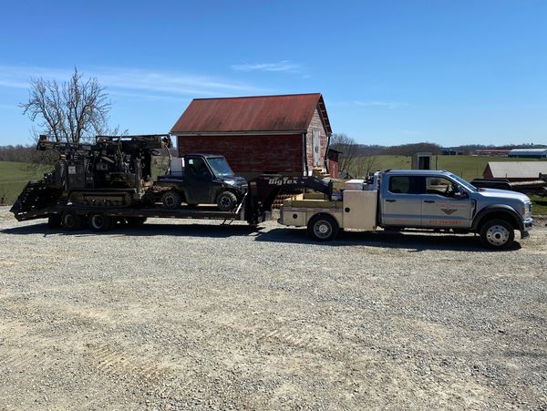 A truck towing a trailer with heavy machinery in a rural setting.