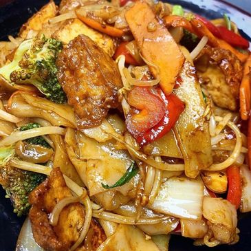 Close-up of stir-fried noodles with vegetables and tofu in a savory sauce.