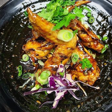 Glazed chicken wings garnished with green onions and fresh herbs on a black plate.